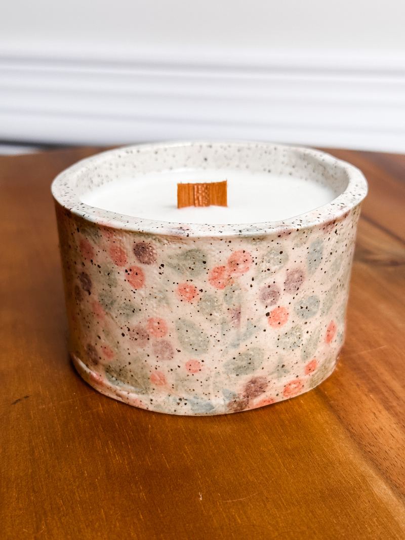 Speckled ceramic candle with a red and green floral pattern among pine branches
